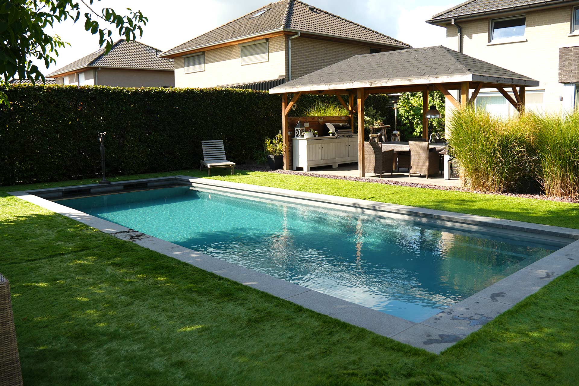 Tuinzwembad met natuurstenen boord en groen gazon